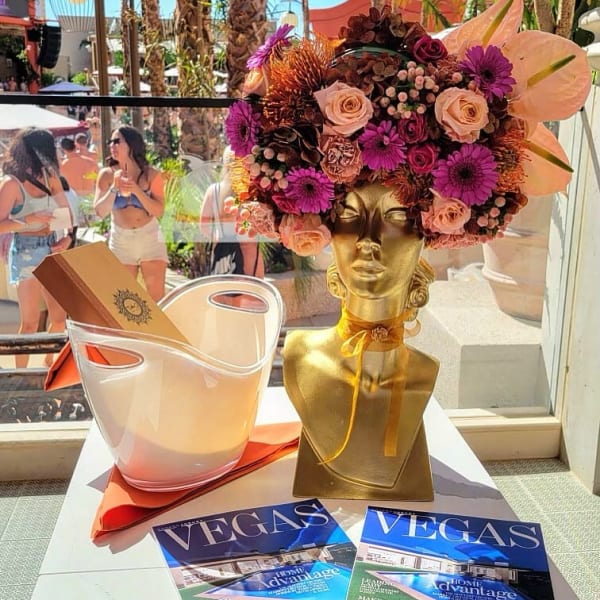 Gold bust vase with a pink and purple floral arrangement beside a clear bucket