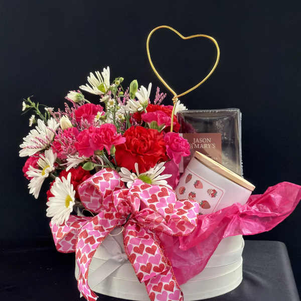 Pink and white flower arrangement with a heart topper and gift items in a round box