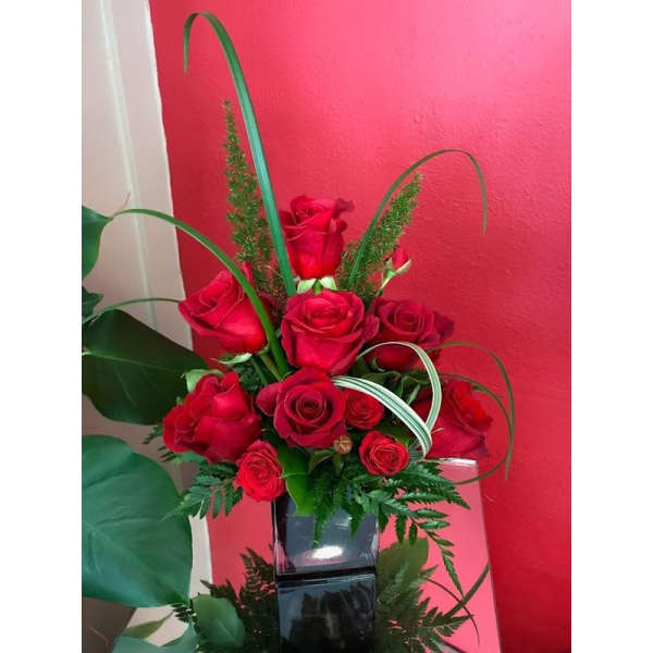 Red roses arranged in a black square vase with curved grass accents