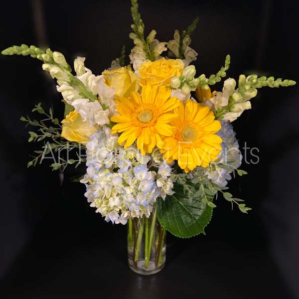 Yellow gerbera daisies and white flowers in a clear glass vase