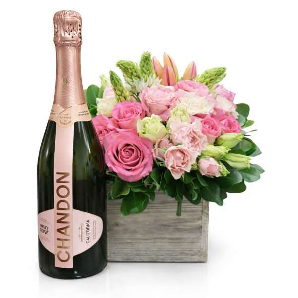 Bottle of sparkling rosé beside pink and white rose arrangement in a rustic wooden box