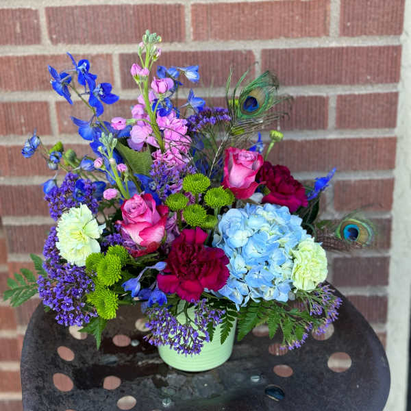 Colorful mixed bouquet in a pale green container with peacock feathers