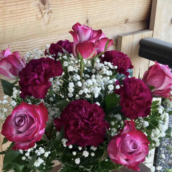 Arrangement of pink roses, deep red carnations, and white filler flowers in a frosted glass vase.