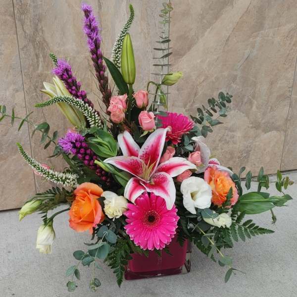 Mixed bouquet with pink lilies, roses, and gerbera daisies in a square vase