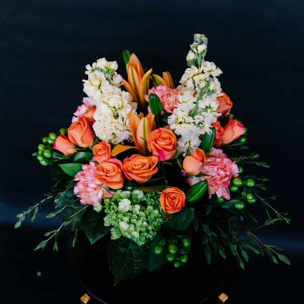 Orange roses and white stock in a black vase