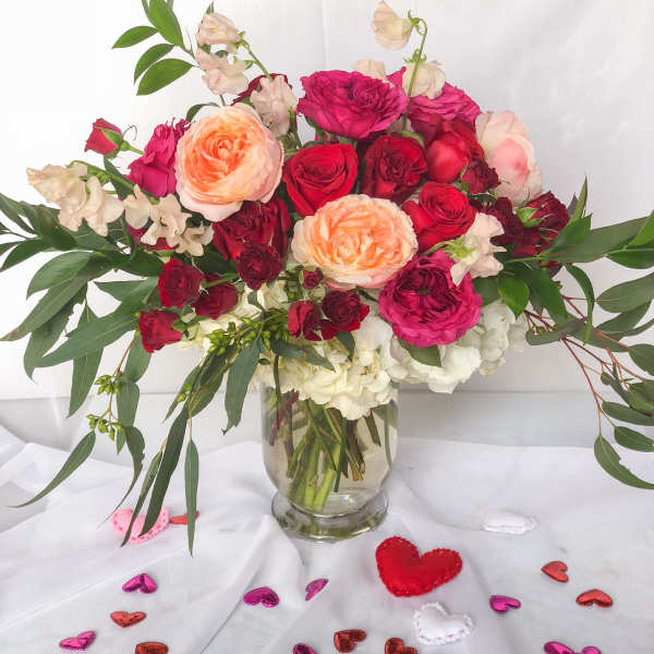 Mixed roses and sweet pea in a clear glass vase with heart confetti
