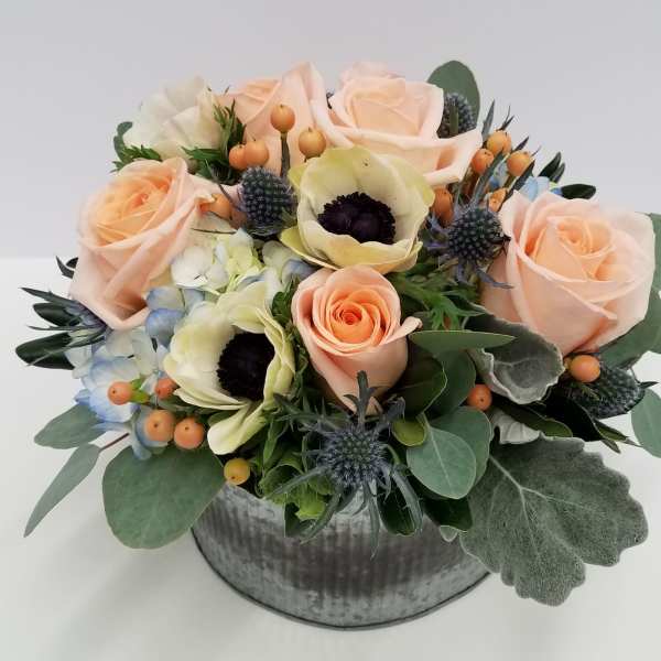 Peach roses and pale blooms arranged in a round metal container