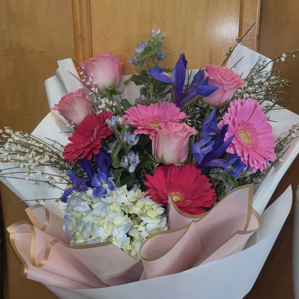 Bouquet of pink roses, gerbera daisies, hydrangea, and blue irises wrapped in pink paper