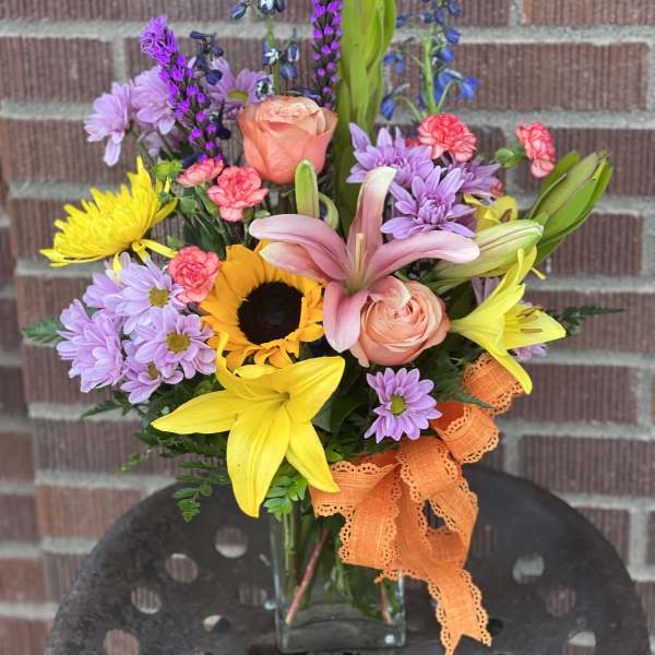 Mixed bouquet with sunflowers, lilies, roses, and purple daisies in a glass vase