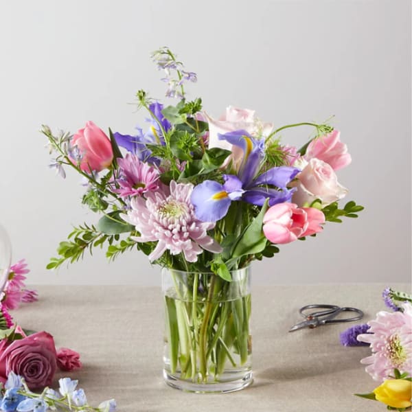 Mixed bouquet of pink, purple, and white flowers in a clear glass vase