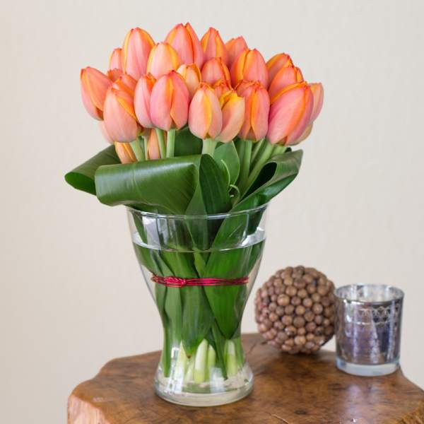 Pink tulips in a clear glass vase with broad leaves