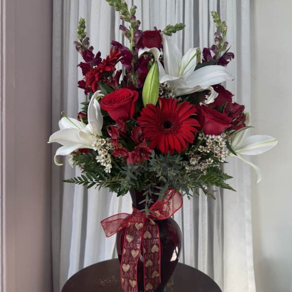 Red and white floral arrangement in a dark vase with a heart ribbon