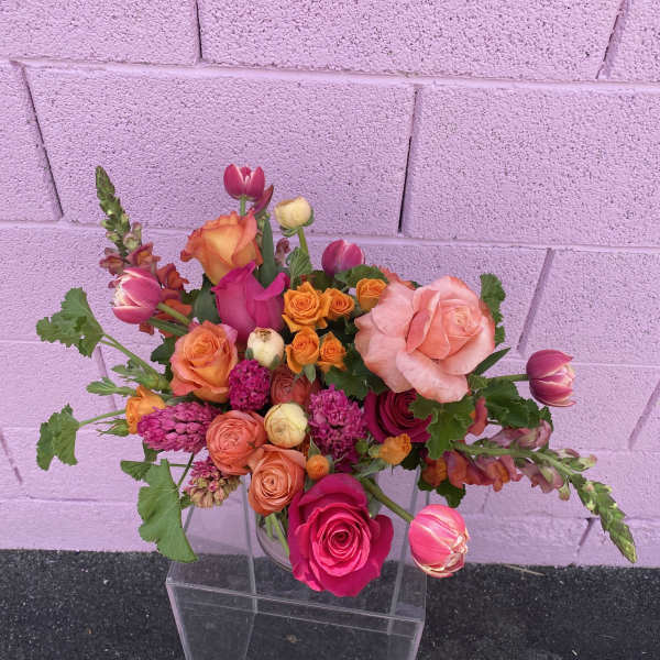 Mixed bouquet of pink, orange, and peach roses in a clear vase