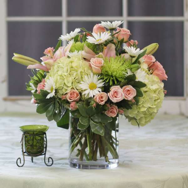 Bouquet of pink roses, white daisies, and green hydrangeas in a glass vase