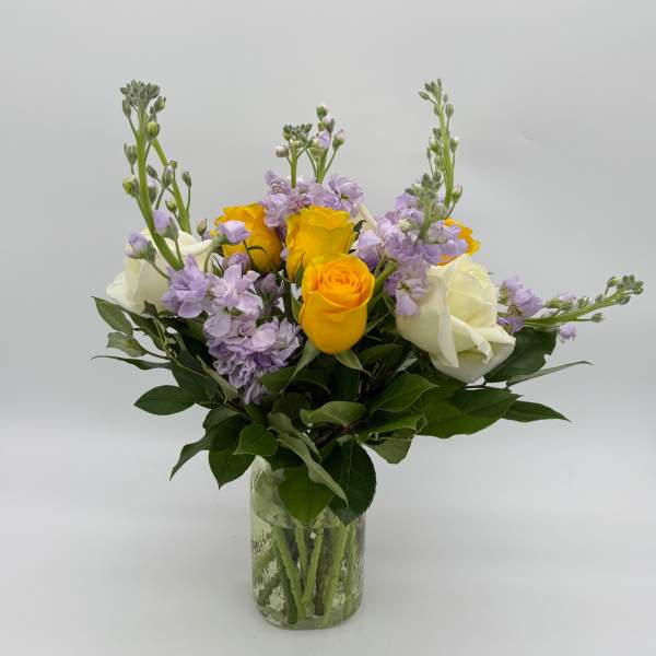 Bouquet of yellow and white roses with lavender flowers in a glass vase