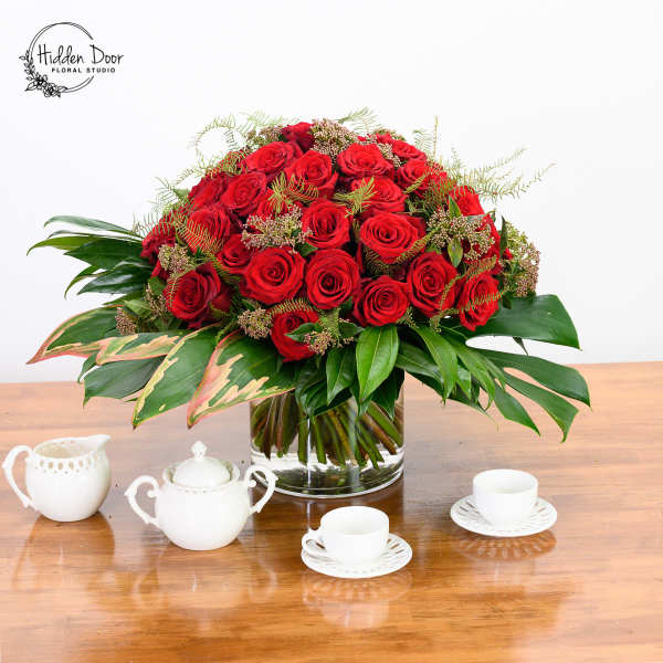 Red rose arrangement in a clear glass vase on a wooden table