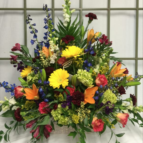 Large mixed flower arrangement in a basket with lilies, gerberas, and delphinium