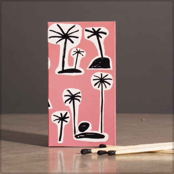Pink matchbox with black palm tree drawings and matches beside it