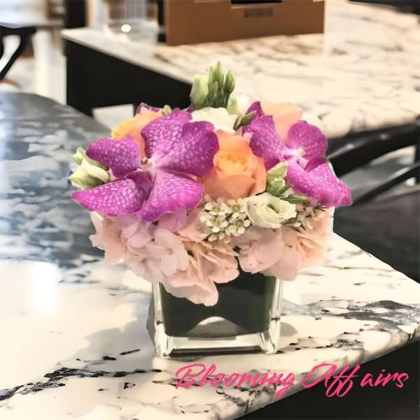 Pink and purple flowers arranged in a square glass vase