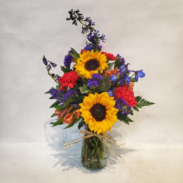 Bouquet of sunflowers, red carnations, and blue flowers in a glass vase