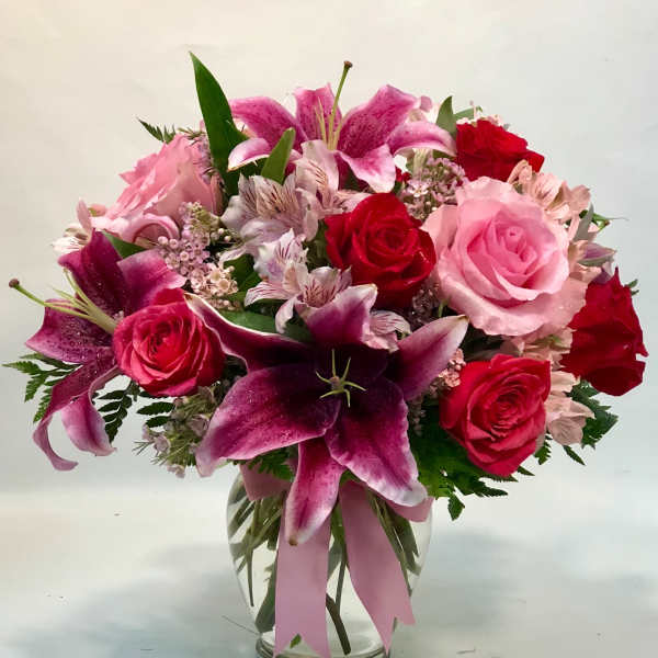 Pink and red roses with lilies in a clear glass vase