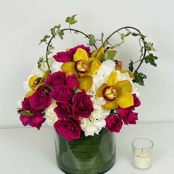 Magenta roses and yellow orchids in a green glass vase with ivy arches