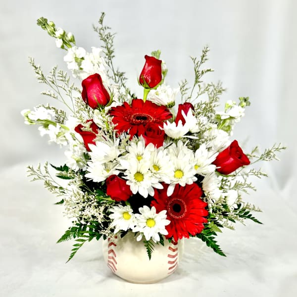 Red roses, red gerbera daisies, and white daisies arranged in a baseball-themed ceramic vase