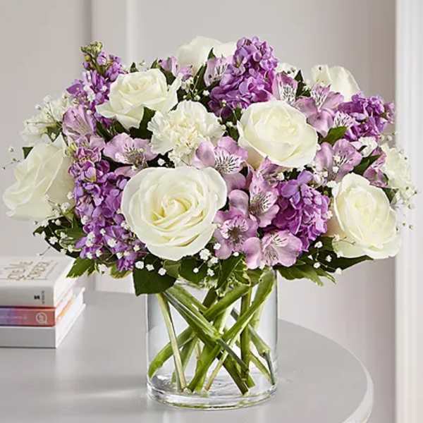 White roses and purple flowers arranged in a clear glass vase