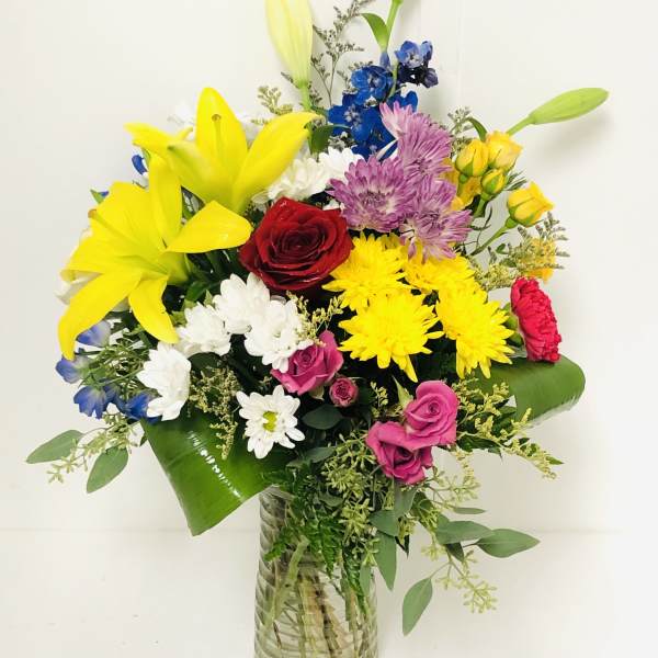 Colorful mixed bouquet in a glass vase with lilies, roses, and daisies