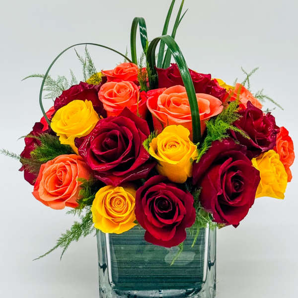 Bouquet of red, yellow, and orange roses in a square glass vase