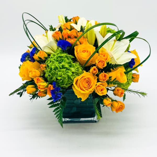 Orange roses and white lilies in a square glass vase