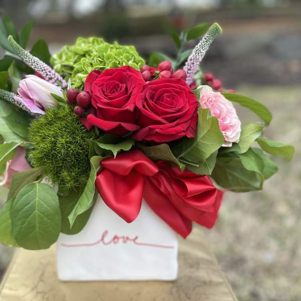 Red roses and pink blooms in a white vase with a red ribbon