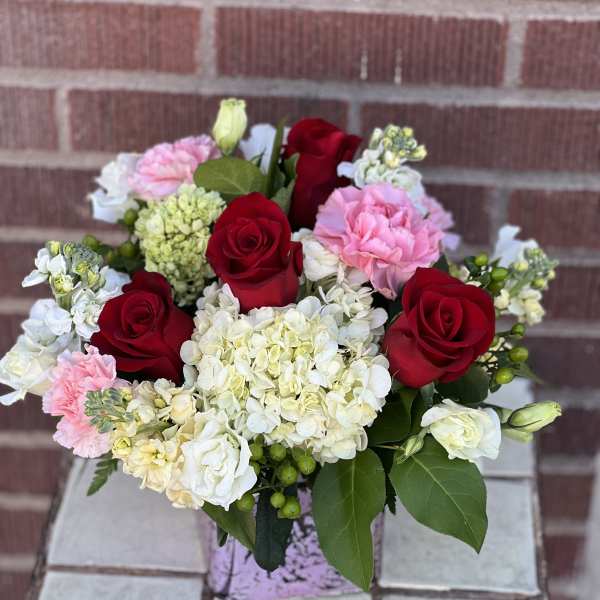 Bouquet of red roses, pink carnations, and white hydrangeas in a vase