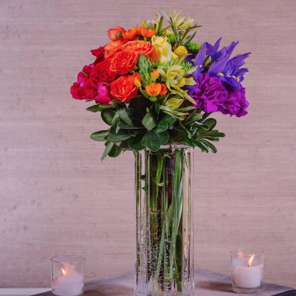 Colorful bouquet in a tall glass vase with candles on either side