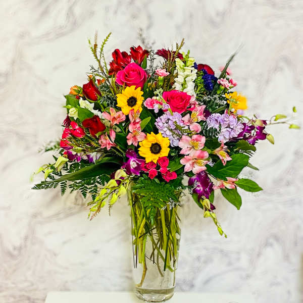 Mixed bouquet of roses, sunflowers, and orchids in a glass vase