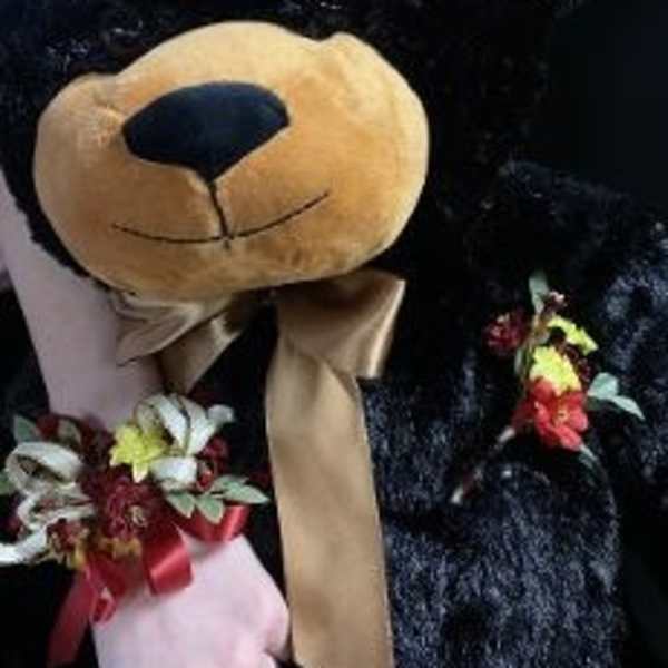 Teddy bear holding small floral accents and a ribbon