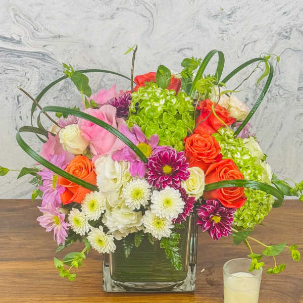 Mixed bouquet of roses, chrysanthemums, and hydrangea in a square glass vase