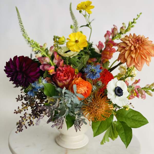 Colorful mixed flower arrangement in a white pedestal vase