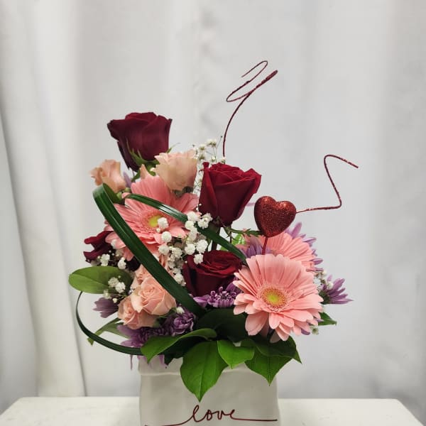 Pink and burgundy flower arrangement in a white box with a heart pick