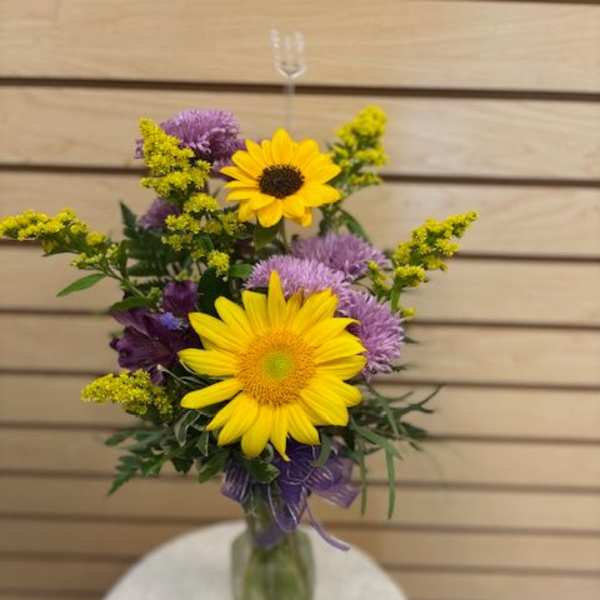 Bouquet of yellow sunflowers and purple flowers in a glass vase