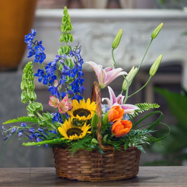 Basket arrangement with sunflowers, lilies, and blue flowers