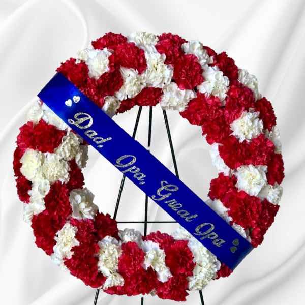 Red and white carnation funeral wreath with a blue memorial sash