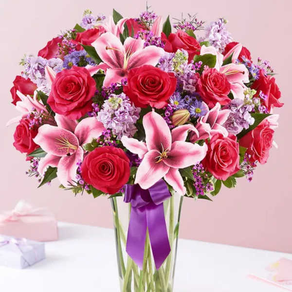 Bouquet of red roses and pink lilies in a clear glass vase with a purple ribbon