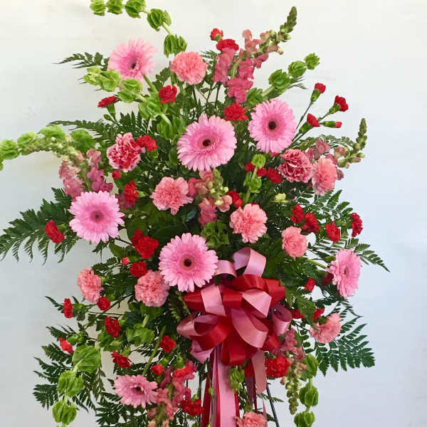 Standing floral spray with pink gerberas, carnations, and red accents