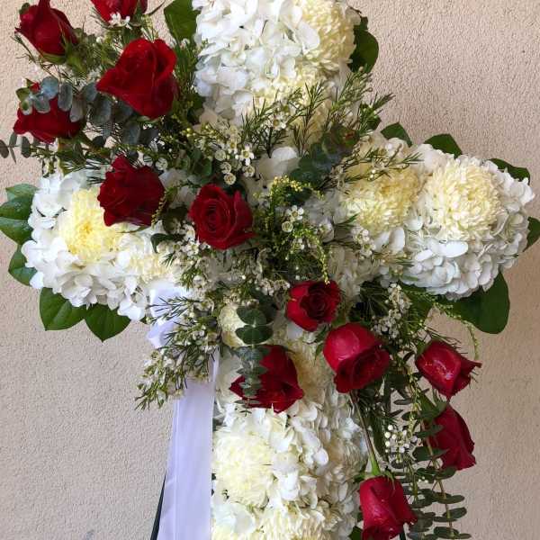 Cross-shaped floral tribute with white blooms and red roses on a stand