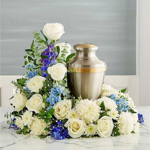 White roses and blue flowers arranged around a metal urn