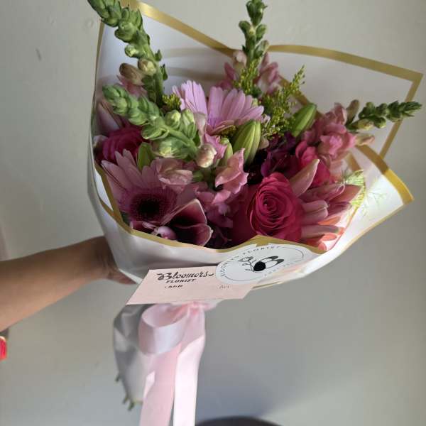Pink mixed flower bouquet wrapped in white paper with a pink ribbon