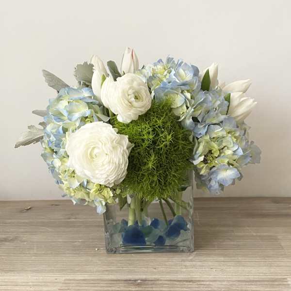 Blue hydrangeas and white ranunculus in a square glass vase
