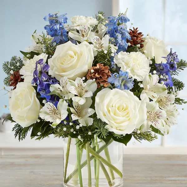 White roses and blue flowers arranged in a clear glass vase