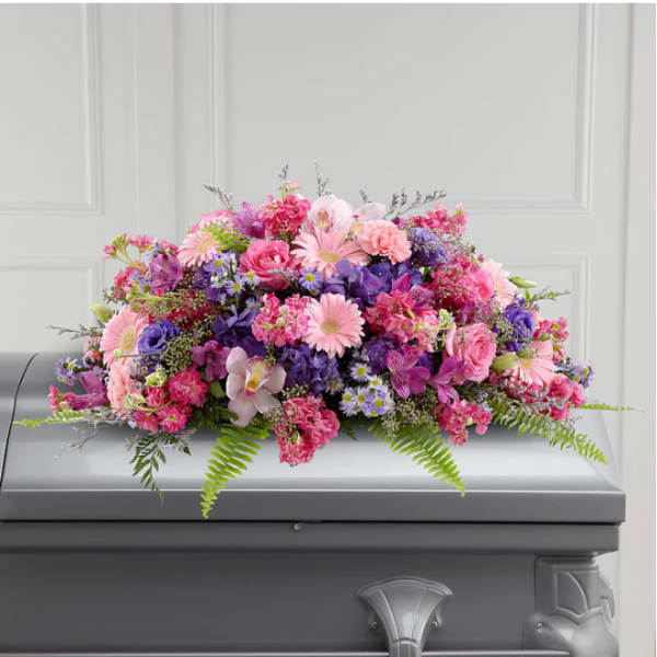 Pink and purple floral casket spray on a gray casket